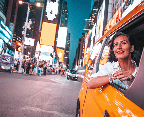 Eine Frau schaut aus dem Fenster eines Taxis, während sie durch die belebten Straßen von Times Square in New York City fährt. Die leuchtenden Werbetafeln und die Menschenmenge schaffen eine lebendige und energiegeladene Atmosphäre.