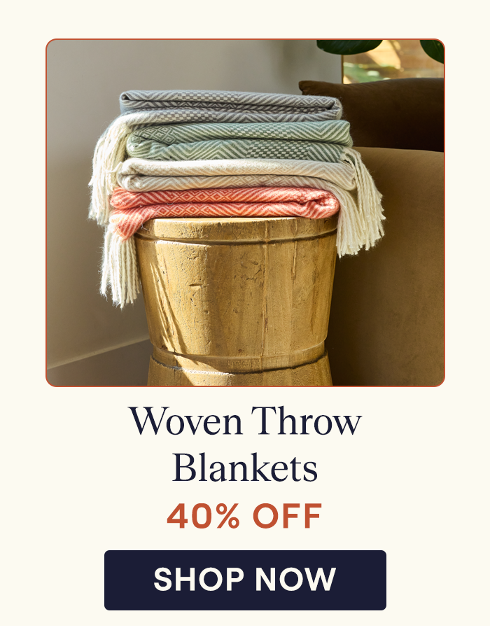 A stack of the Woven Throw blankets on a stool in Brick, Storm, Almond, and Juniper colorways